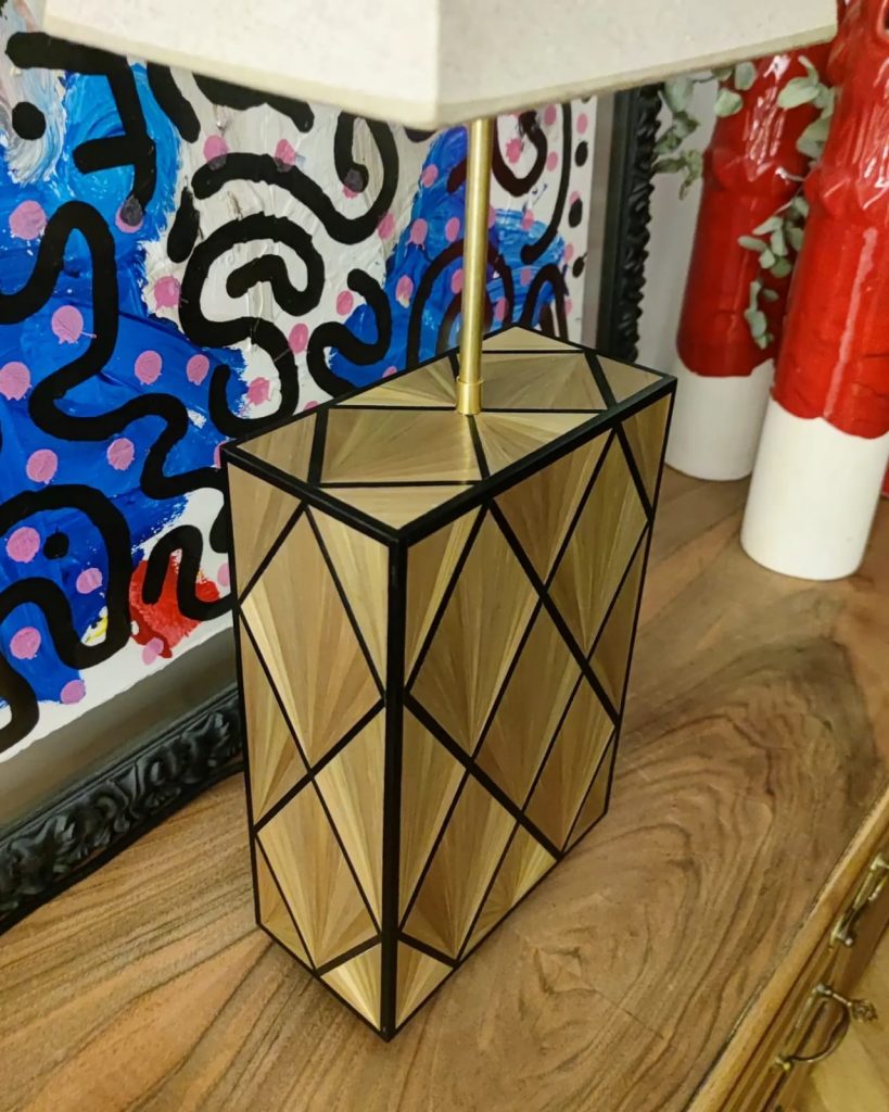 Lámpara con patrón geométrico, realizada en paja dorada y negra. El interior de los rombos con motivos en palmera.