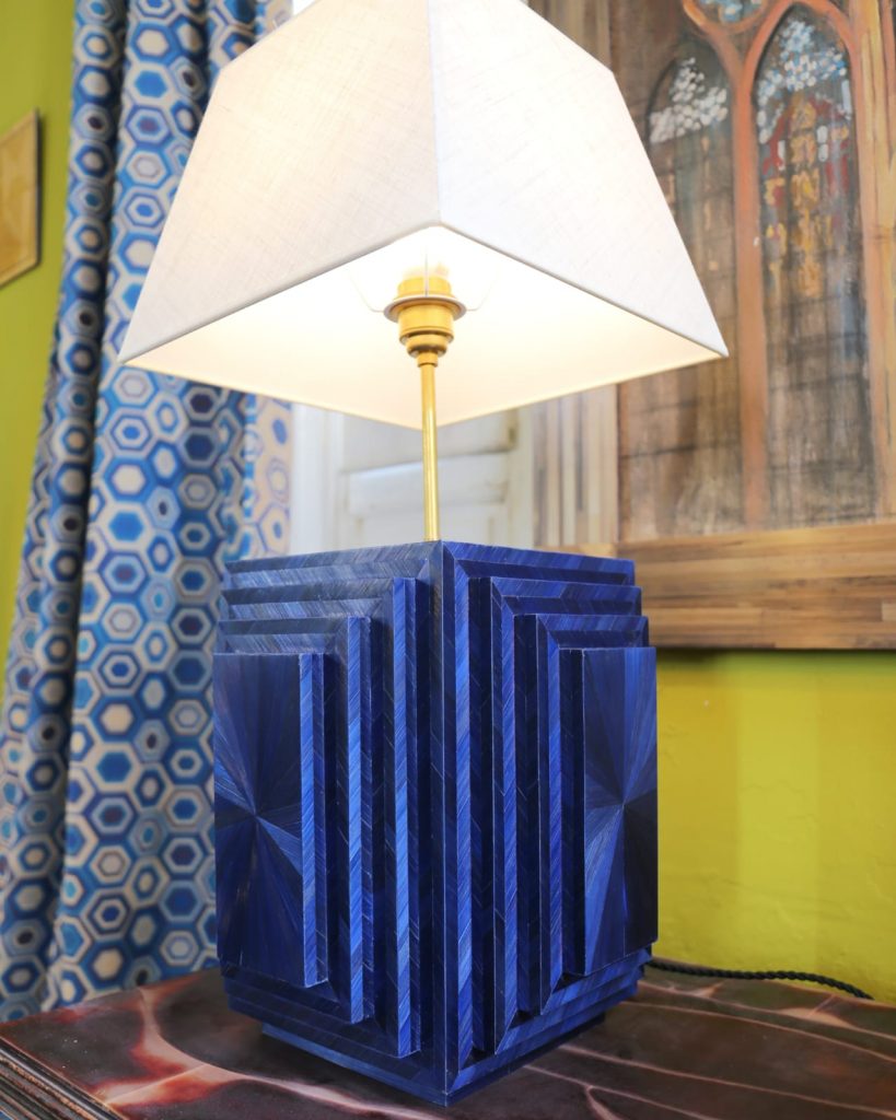 Lámpara de mesa, inspirada en la pirámide escalonada de Saqqara, realizada con paja de centeno azul profundo. Frontales con patrón "sol" y perfiles en espiga bidireccional, creando un juego de luces fabuloso. 